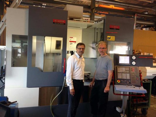 Två män står i en verkstad bredvid en stor industriell cnc-maskin.